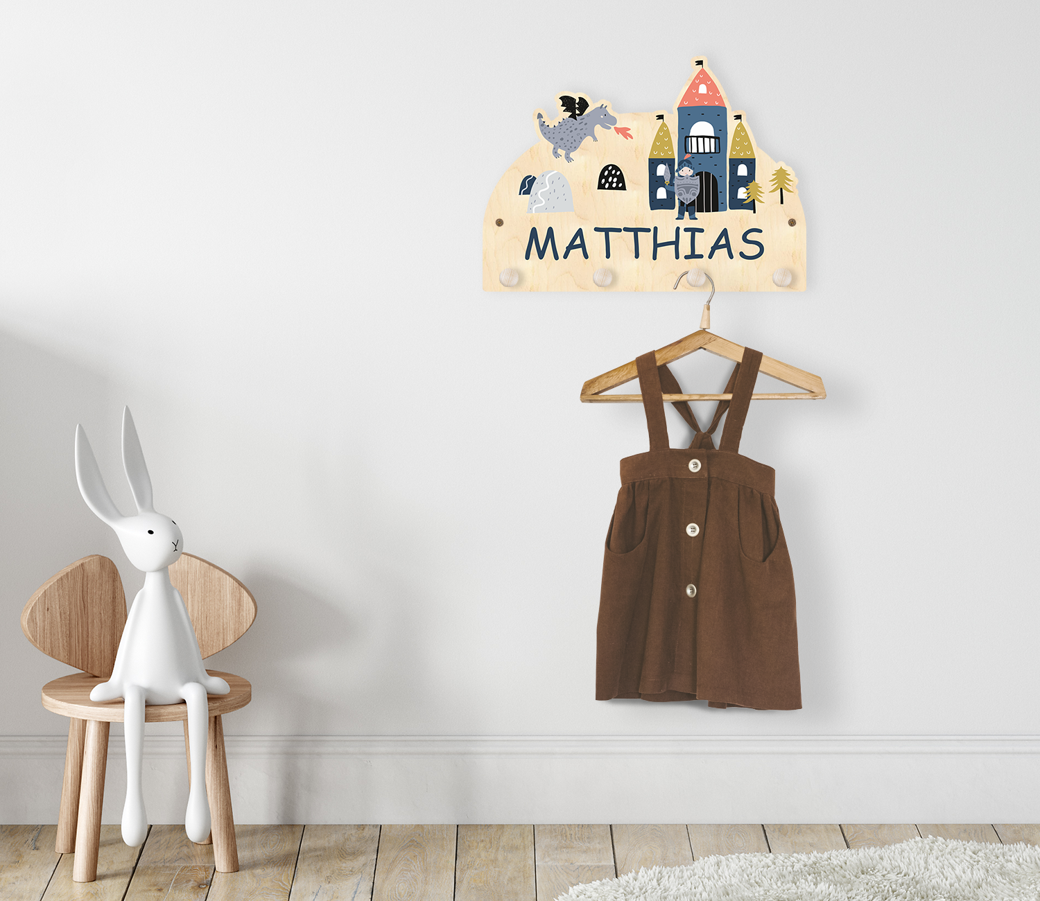 Garderobe mit Ritterburg und Namen aus Holz im Kinderzimmer. An der Garderobe hängt ein Kleiderbügel mit einem Kleidungsstück.