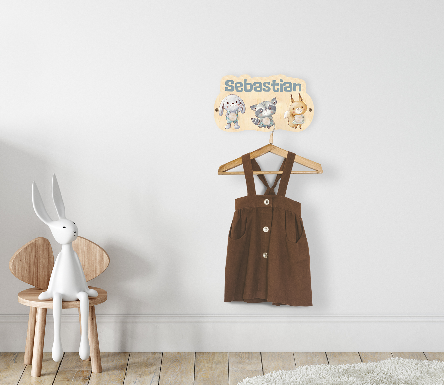 Kindergarderobe, mit eigenem Name personalisiert und den Tieren Hase, Waschbär und Fuchs, montiert an einer Kinderzimmerwand. An der Garderobe hängt ein Kleiderhaken mit einem Kleidungsstück.